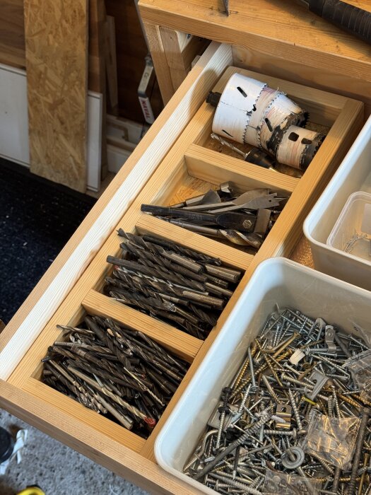 En verktygslåda med borrar och bits organiserade i fack, tillsammans med en plastlåda fylld med skruvar och clips.