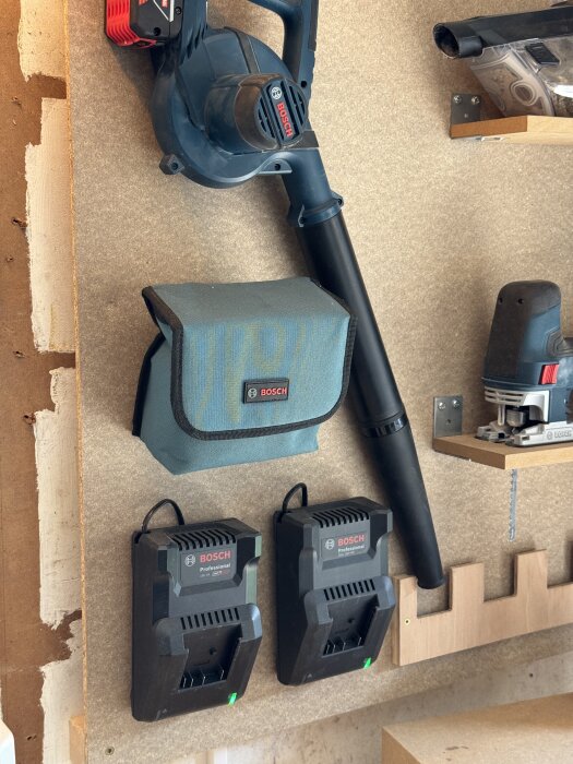 Väggmonterad verktygsförvaring med Bosch-blåsare, laddare och verktygspåsar i ett organiserat garage.