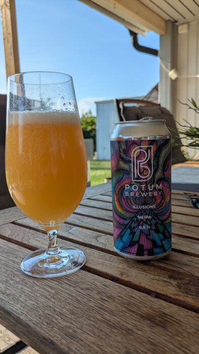 Glas med gulorange öl bredvid en burk från Potum Brewery på ett trädäck i solsken.