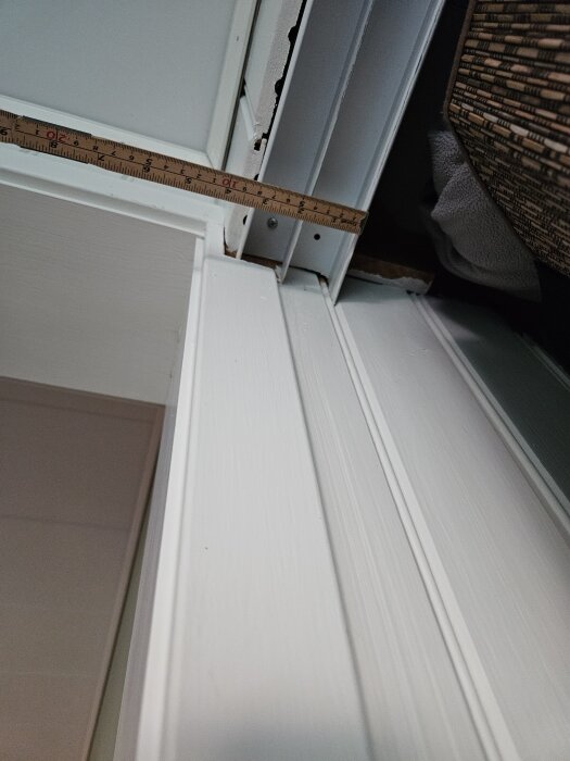 Mätning av dörrkarm med trälinjal vid installation av skjutdörrsskena i hall, vit yta och dörrspår synliga.