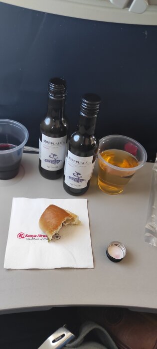 Två små flaskor vin, en plastkopp med röd dryck, en kopp med guldig dryck, och en halv uppäten smörgås på en Kenya Airways-servett.
