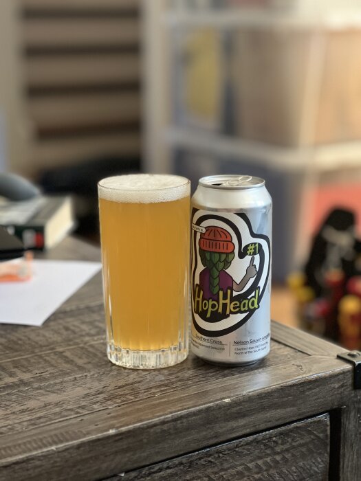En burk med drycken "HopHead" bredvid ett fyllt glas står på ett bord.
