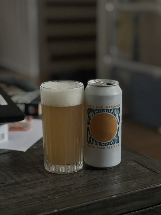 Ett glas med skummande öl bredvid en burk Stigbergets Göteborg IPA på ett bord.