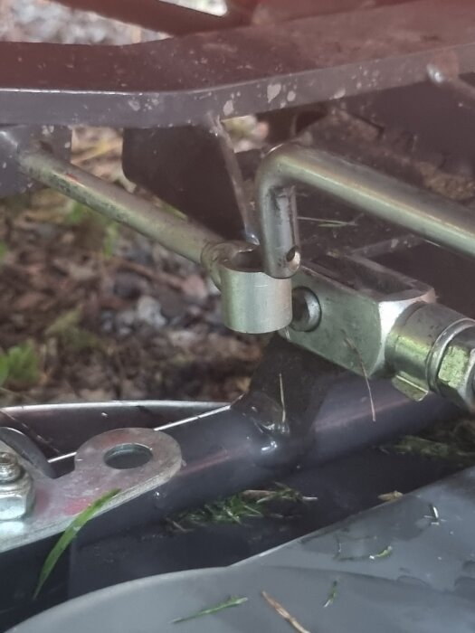 Närbild på del av Husqvarna Rider 13, fokus på en metallpinne och hål på klippdäcket. Gräsrester och smuts syns runt om.