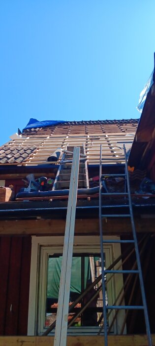 Takreparation med stegar och verktyg synliga, del av ett hus.