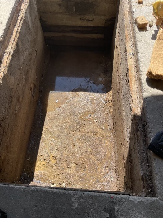 Smörjgrop i garage med vattensamling på botten, visar tydliga tecken på vattenläckage underifrån i en betongmiljö.