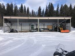 Självbärande plåttak över förråd eller carport med olika föremål under, omgiven av snö och skog i bakgrunden.