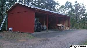 Röd byggnad med självbärande plåttak, skog i bakgrunden.