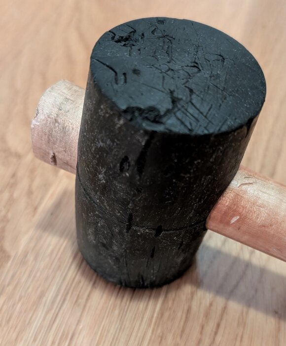 Gummiklubba med sprött och sprucket gummi på huvudet, använt i ca 10-15 år, ligger på ett trägolv.