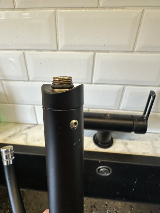 Svart köksblandare med avbruten infästning framför vita kakelplattor.