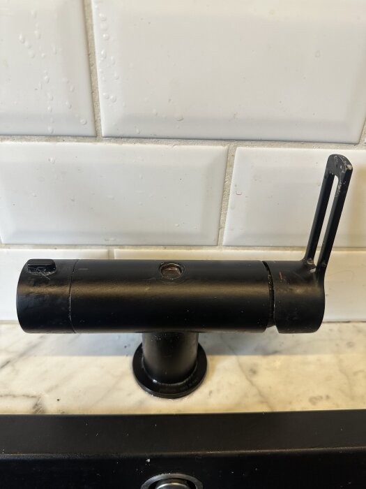 Svart, löst köksblandare monterad på en marmoryta framför vita kakelplattor.