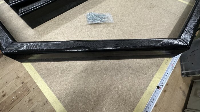 Svarta träramar i en oktagonal form på ett arbetsbord, med en påse skruv och en måttstock i närheten.