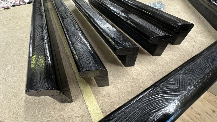 Svarta, nylackade träbitar i vinkel, placerade på ett grovslipat träbord, redo för montering i ett strategispelprojekt.