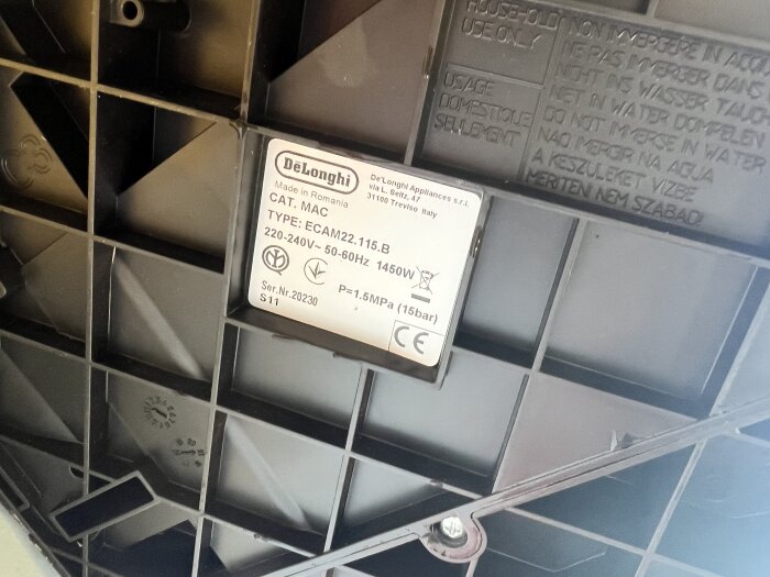 Etikett på undersidan av DeLonghi Magnifica S kaffemaskin, anger modell, strömspänning och tryckinformation.
