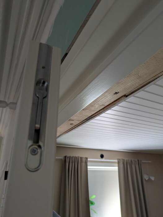 Pardörr (London) i vit ram sedd från sidan, med synlig insexskruv i karmen, del av rum med takpanel och gardiner i bakgrunden.