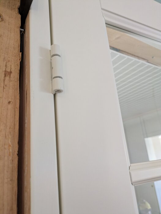 Närbild på ett vitt dörrgångjärn monterat på en pardörr från Bauhaus, fäst vid en träram.