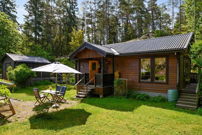 Trähus från 1983 i skogsmiljö med trädäck, utemöbler och parasoll, erbjuds för nedmontering och bortforsling, Botkyrka kommun.