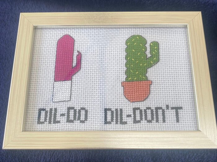 Broderi med två kaktusar i ram, en rosa med texten "DIL-DO" och en grön i kruka med texten "DIL-DON'T".