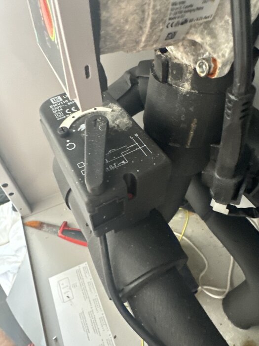 Närbild på en Wilo pump och dess reglage i ett pannrum, med synliga elsladdar och en rörkoppling. En såg skymtas i bakgrunden.