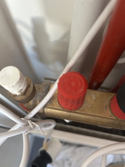 Rörsystem med röda och vita ventiler, kopplade till en värmepanna, med kablar inblandade.