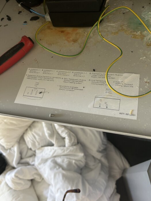 Elektrisk anslutning med diagram, gula och gröna kablar samt en elektrisk skruvmejsel. Instruktioner för värme- och kylsystem syns på pappersinstruktionen.