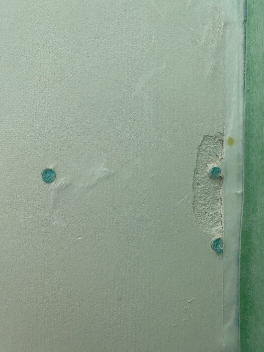 Skada på gipsskiva med exponerad gips och delaminerat glasfiberskikt, omgiven av fastsatt Kerasafe-folie.