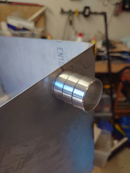 Närbild på punkt- och svetsad metalltank med utstickande armatur i verkstadsmiljö.