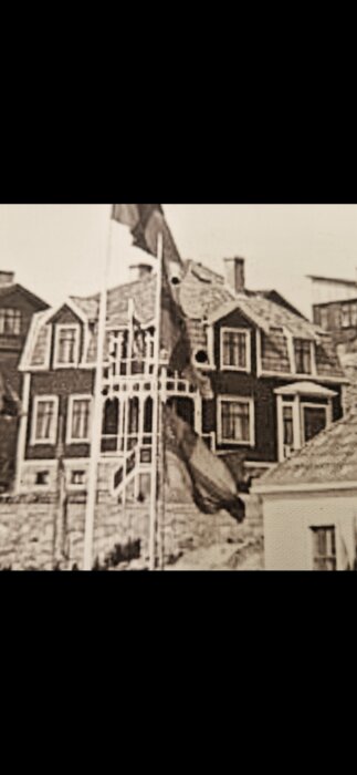 Gammalt foto av ett hus med nya fönster i olika dimensioner och flagga i förgrunden. Taken ur unik vinkel för att framhäva känslan.