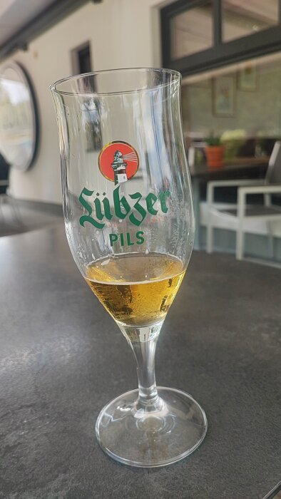Ett halvtomt glas med Lübbzer Pils-öl står på ett bord med suddig bakgrund, tagen på en camping i Schwerin, Tyskland.