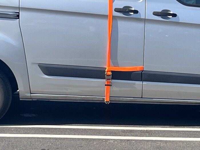 En vit skåpbil med orange remmar fastsatta på sidan, vilket antyder hemmagjord konstruktion.