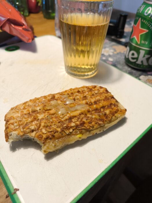 Panini med röktskinka och ost på skärbräda bredvid ett glas dryck och en ölburk.