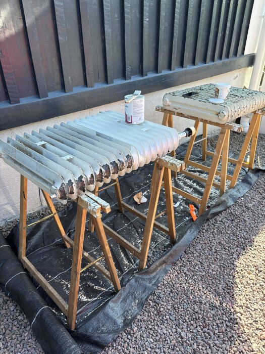 Renoverade element på träbockar med målarfärg i förgrunden, placerade utomhus mot en svart vägg.