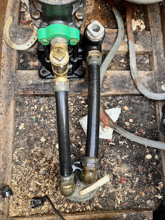 VVS-rör och kopplingar med kondens och pölar, eventuellt läckage under Grundfos CPE-60 pump i en borrad brunn, omgivna av trä och skräp.