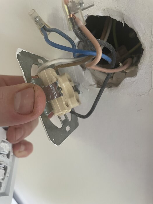 Hand håller elektrisk kopplingsplatta med flera exponerade ledningar i taket.