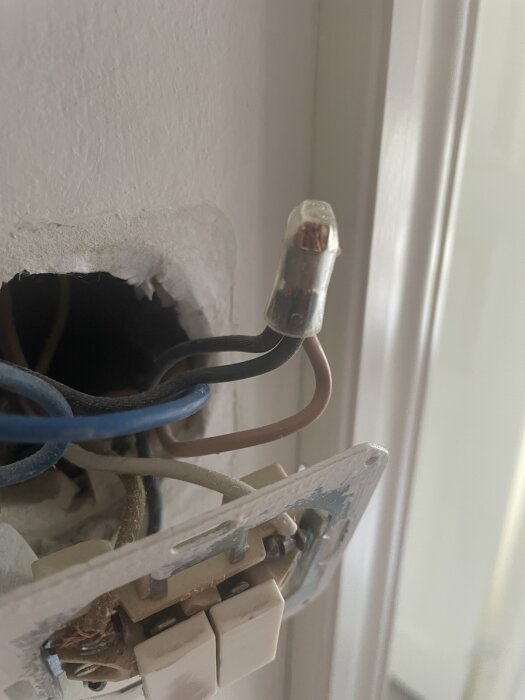 Elektriska kablar och kopplingar i en vägg med synliga färgade ledningar och en anslutningsplint.