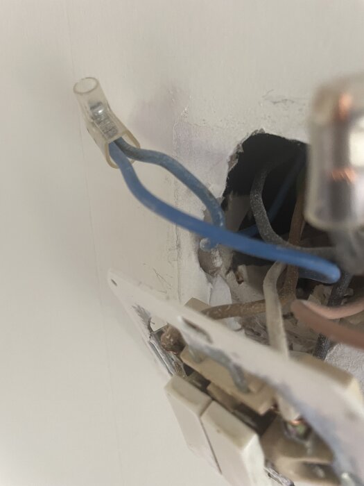 En vägg med en exponerad elektrisk koppling och flera synliga ledningar i olika färger, inklusive en blå ledning.