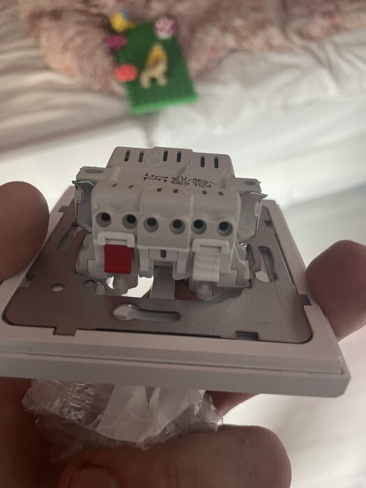 Närbild av en elektrisk kopplingsenhet med flera anslutningar och en röd låsning, hålls i handen. Bakgrunden är suddig.