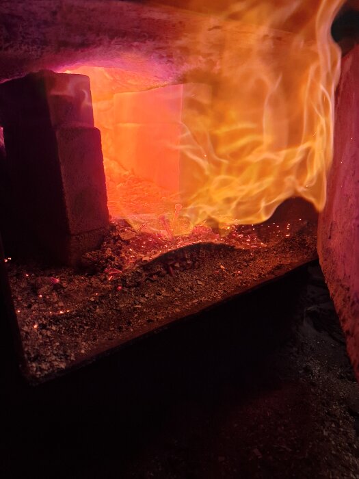 Brinnande lågor i en förbränningskammare, med glödande kol och orange eldflammor.