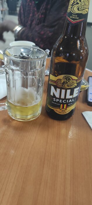 Flaska och glas med lokal öl, Nile Special från Uganda, på ett bord.
