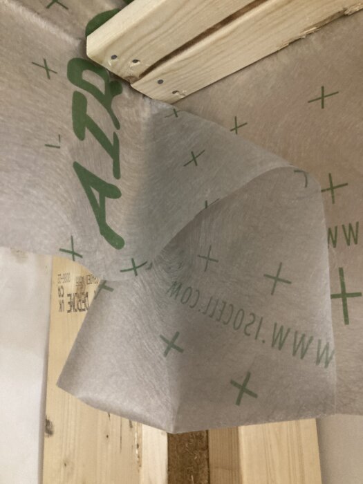 Diffusionsöppen ångbroms i hörn med flera lager överlappande material, monterat på träpanel.