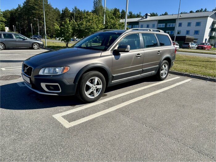 SUV parkerad på asfalterad parkeringsplats en solig dag, med bakgrund av skog och moderna byggnader.