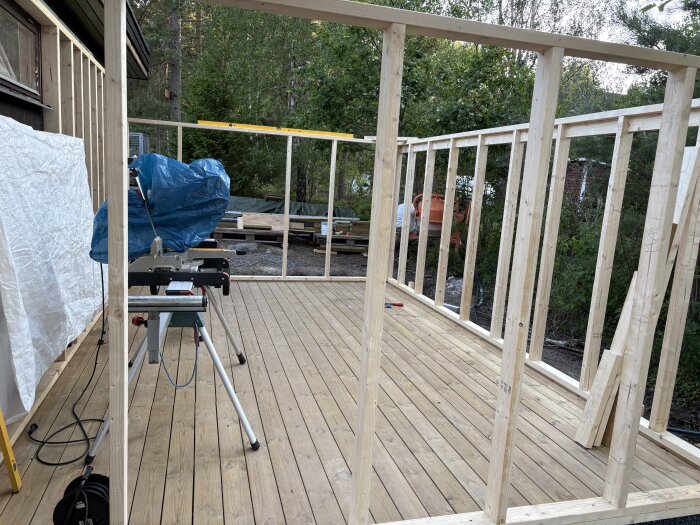 Stomme till kallförråd under uppbyggnad med träbjälkar och golv, omgiven av träd. En arbetsstation med blå täckplast syns till vänster.