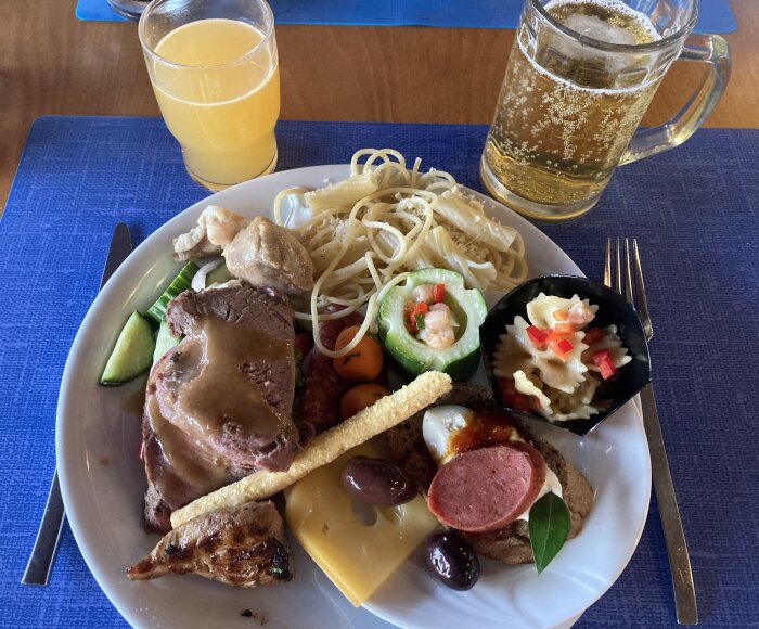Tallrik med buffémat inklusive rostbiff, pasta, grönsaker och drycker på ett bord.