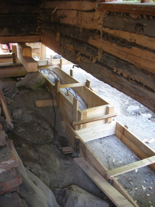 Betongformar av trä placerade på en grusbädd bredvid ojämnt berg, del av grundläggning i renoveringsprojekt.