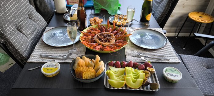 Kräftskiva med kräftor, paj, kex, ost, bröd, melon, jordgubbar, passionsfrukt och champagne på ett dukat bord.