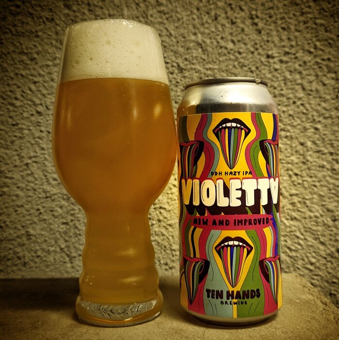 Ett glas öl bredvid en färgglad burk med etiketten "Violetta DDH Hazy IPA" från Ten Hands Brewing.