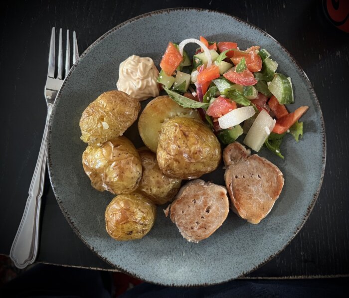 Tallrik med ugnspotatis, köttbitar, grönsallad med paprika och lök, samt en klick beasås.
