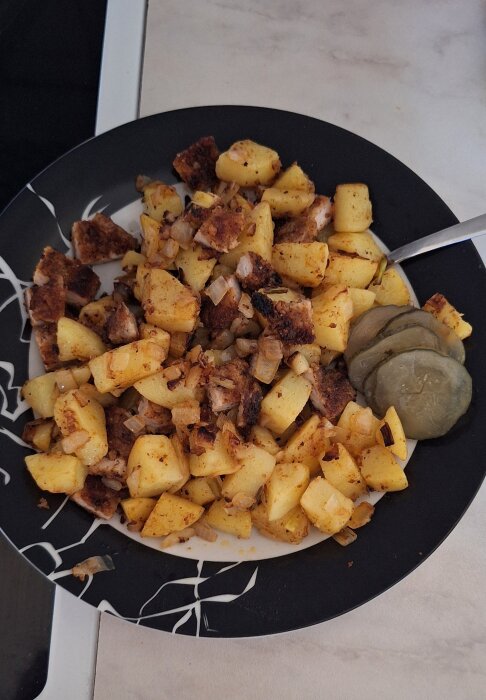 Hemlagad pytt av snitzel, stekt potatis och lök med inlagd gurka på en tallrik.