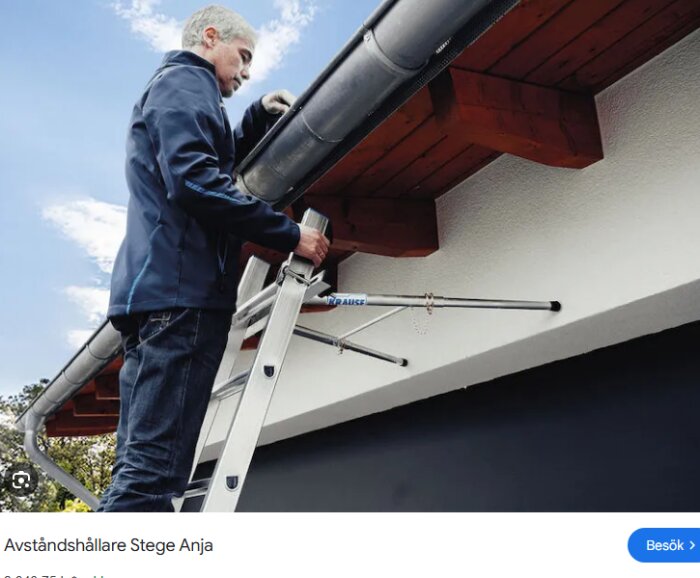 Person står på en stege och arbetar med en hängränna under ett tak med röda takbjälkar.