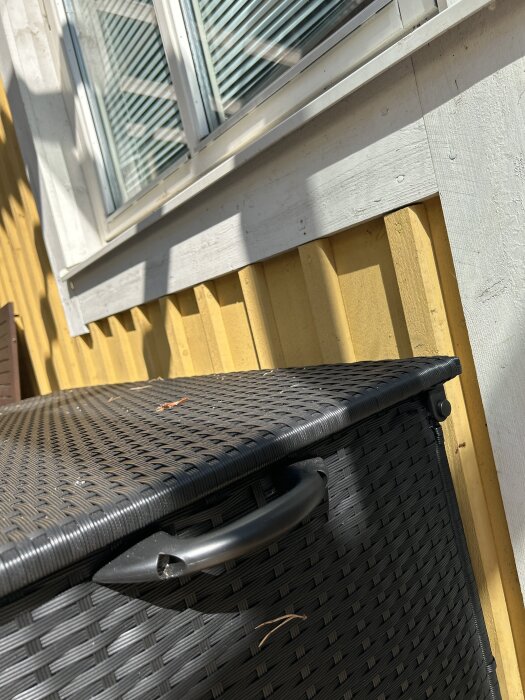Vitmålat takskägg mot gul träpanel vid fönster, med en svart korg i förgrunden.